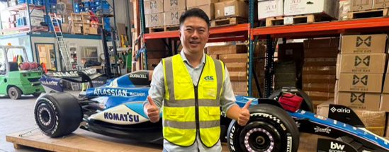 CTS-Mitarbeiter in Warnweste neben einem Formel-1-Showcar in einem Lager